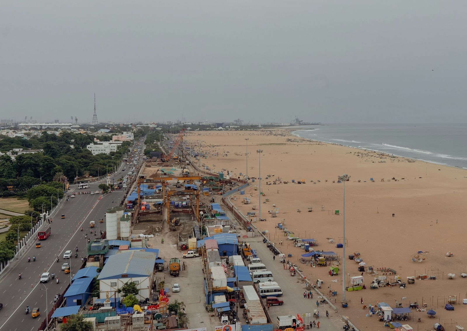 An overview of Marina Beach in Chennai with people, shops, road and vehicles in view.