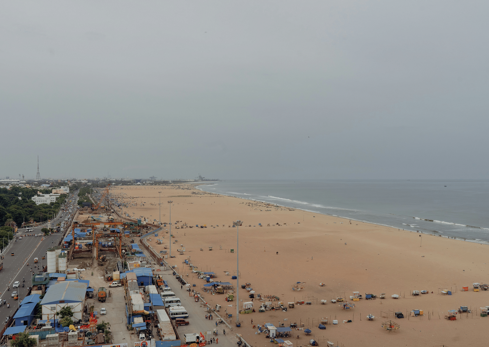 An overview of Marina Beach in Chennai with people, shops, road and vehicles in view.
