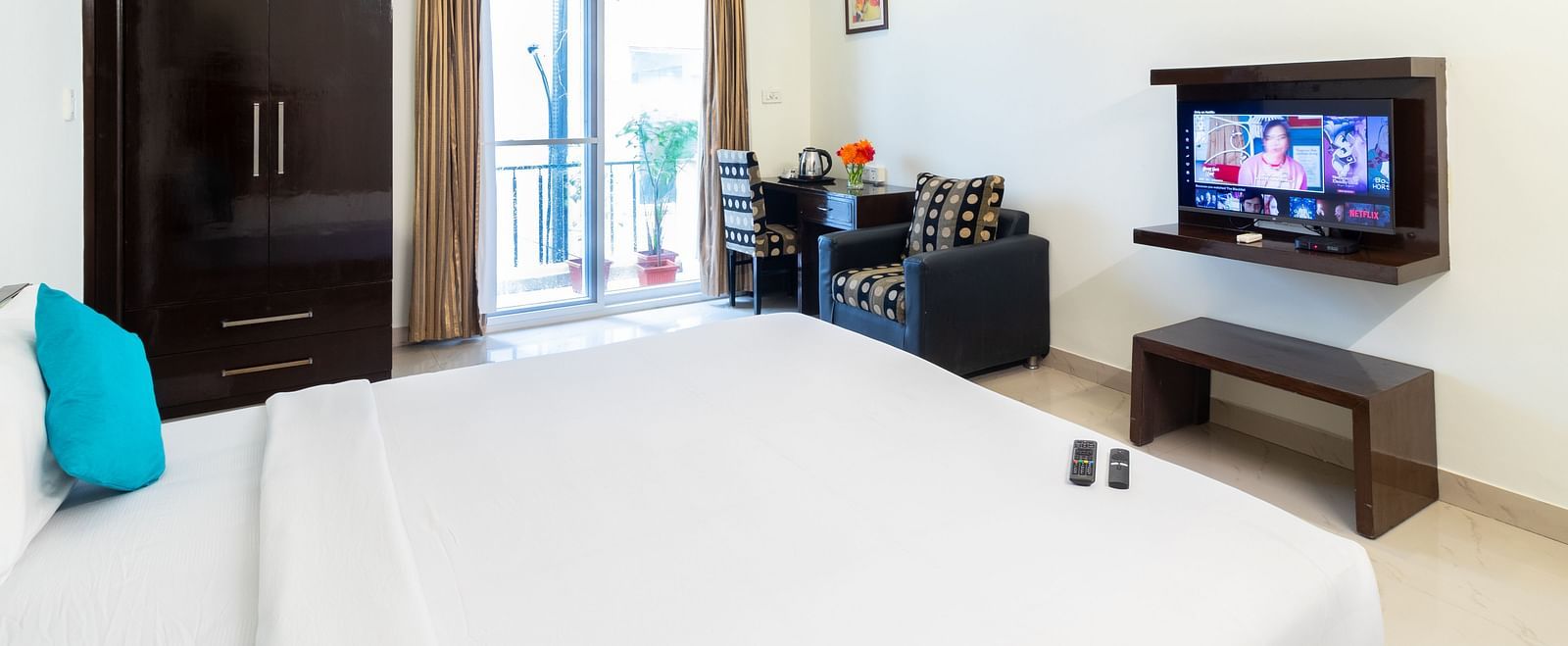 A room with a double bed, a flat-screen TV, a wardrobe, a sofa, and a work desk and chair at Sanctum Suites Domlur, Bangalore.