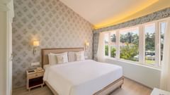 A double bed with side tables, lamps and pillows on the bed inside the suite - Heritage Village Resorts & Spa, Goa