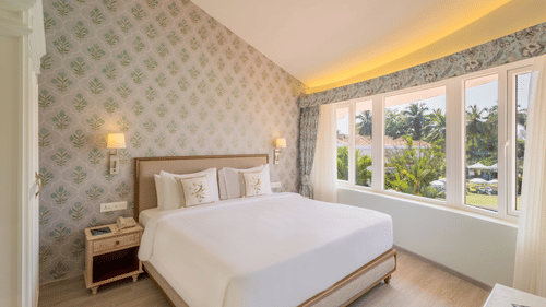 A double bed with side tables, lamps and pillows on the bed inside the suite - Heritage Village Resorts & Spa, Goa
