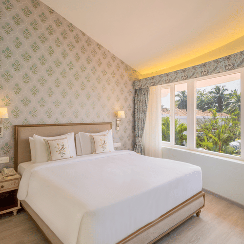 A double bed with side tables, lamps and pillows on the bed inside the suite - Heritage Village Resorts & Spa, Goa