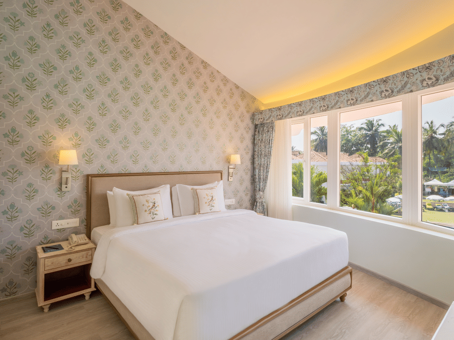 A double bed with side tables, lamps and pillows on the bed inside the suite - Heritage Village Resorts & Spa, Goa