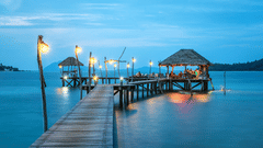 A pier leading to gazebo with lights on the ledge and evening sky in the background
