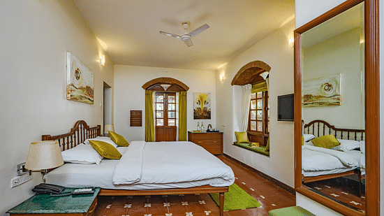A double bed seating area next to the window and a mirror inside Mitras - River View - River View room at neemrana s three waters
