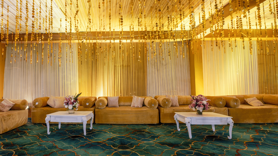 A lounge area featuring long sofas, small white coffee tables, and gold hanging ceiling drapes at Garh Govind.