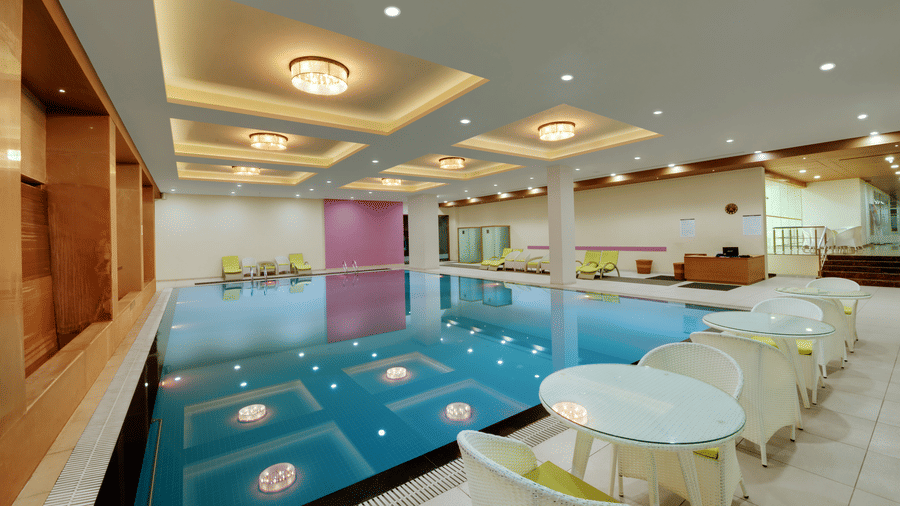 Indoor swimming pool with lounge chairs at Narayani Heights Hotel & Resorts, Ahmedabad.