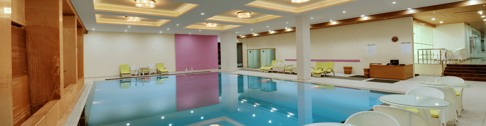 Indoor swimming pool with lounge chairs at Narayani Heights Hotel & Resorts, Ahmedabad.