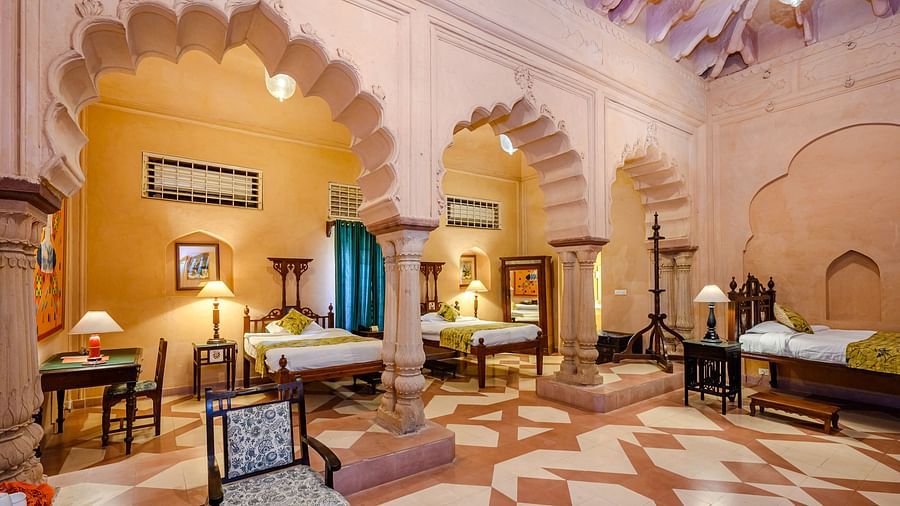A room with multiple beds, arched doorways, tables, chairs, and a patterned floor at Tijara Fort-Palace - 19th Century, Alwar.