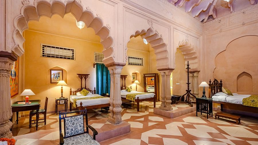 A room with multiple beds, seating, and arched architectural details at Tijara Fort-Palace - 19th Century, Alwar.