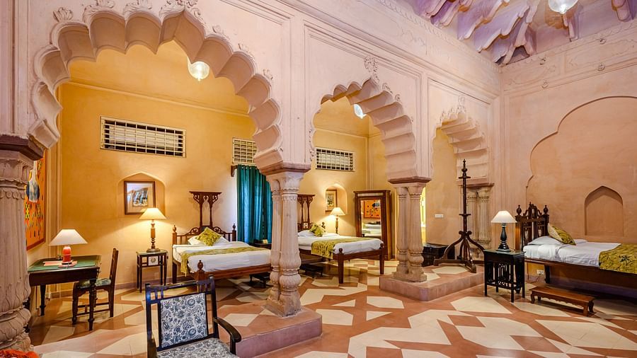 A room with multiple beds, seating, and arched architectural details at Tijara Fort-Palace - 19th Century, Alwar.
