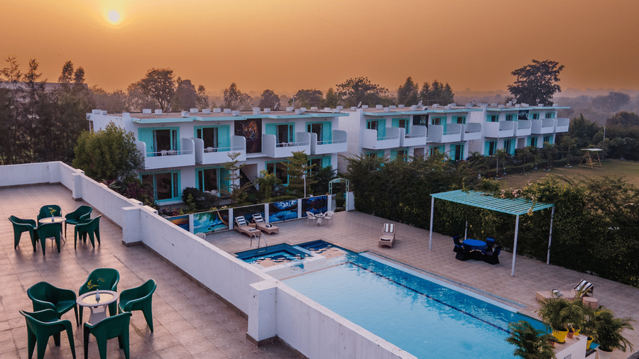 Facade of the Vedikant Resorts The Mallard Corbett featuring a terrace with seating area, a two storey building which has rooms, a swimming pool surrounded by trees.