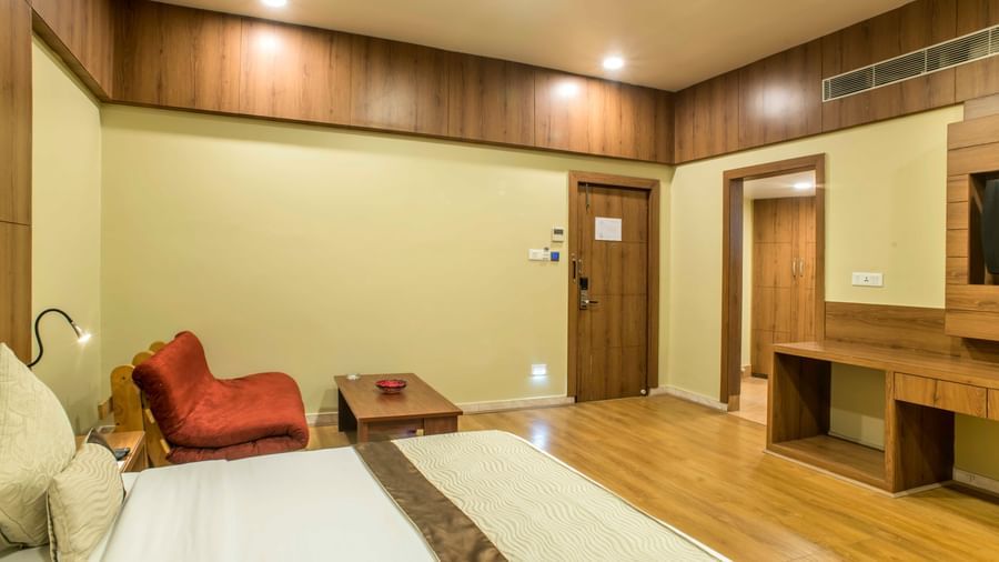 Spacious hotel room with a king size bed, a red armchair, and a wooden entertainment unit at The Citi Residenci Hotel Durgapur