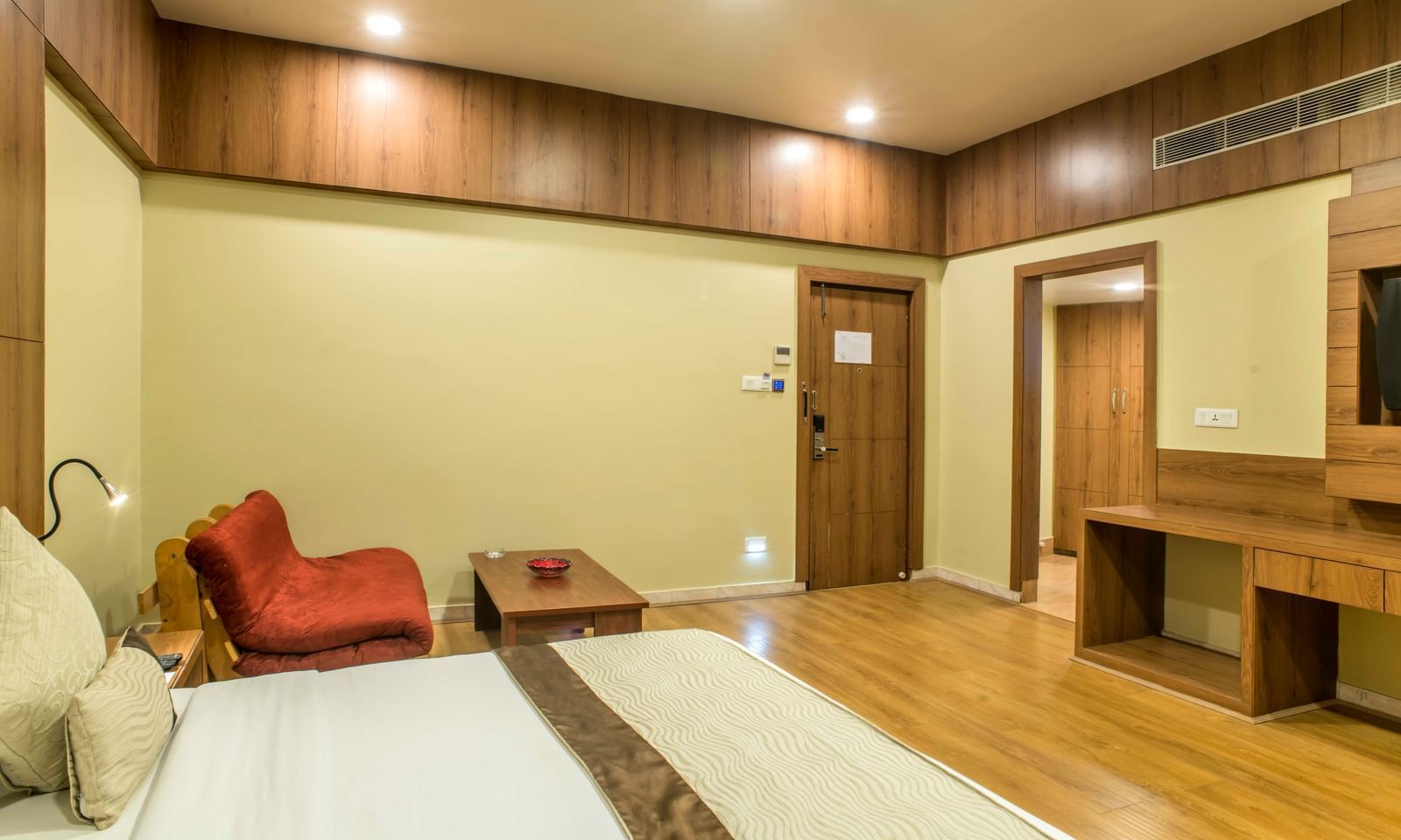 Spacious hotel room with a king size bed, a red armchair, and a wooden entertainment unit at The Citi Residenci Hotel Durgapur