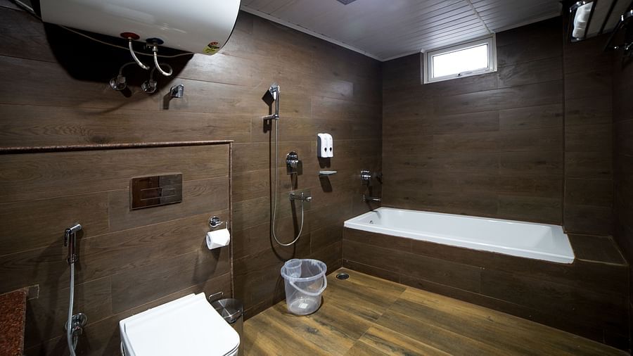 Modern bathroom with dark wooden walls and flooring, featuring a bathtub, wall-mounted shower, toilet, water heater, and a plastic bucket placed near the shower area - Yashshree Lachen.