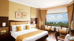 A king sized bed in a bedroom at The Retreat Hotel & Convention Centre with a picturesque view,  a desk, three chairs, a tea table and bedside table.