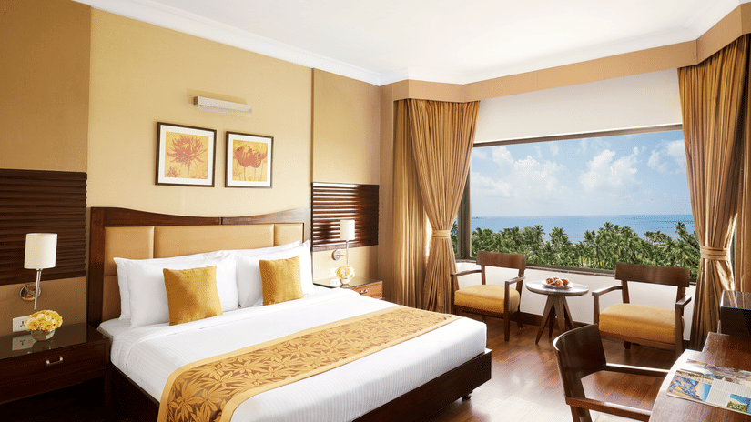 A king sized bed in a bedroom at The Retreat Hotel & Convention Centre with a picturesque view,  a desk and chair, two chairs, a tea table and bedside table.