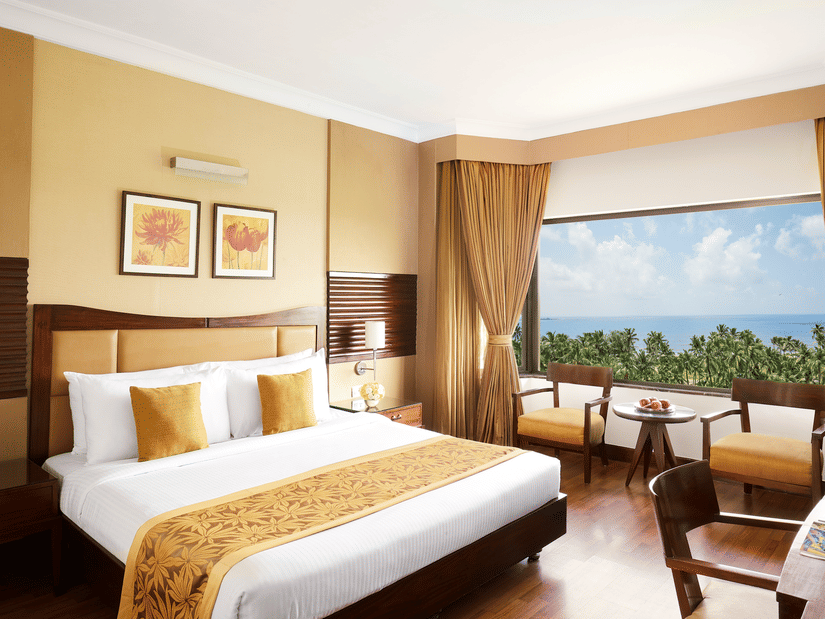 A king sized bed in a bedroom at The Retreat Hotel & Convention Centre with a picturesque view,  a desk, three chairs, a tea table and bedside table.