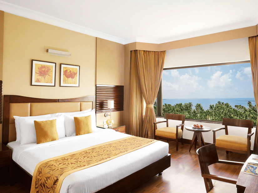 A king sized bed in a bedroom at The Retreat Hotel & Convention Centre with a picturesque view,  a desk, three chairs, a tea table and bedside table.