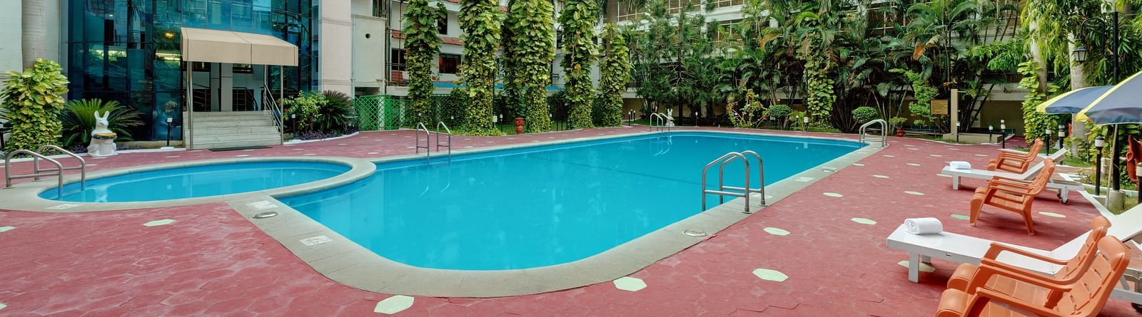 A swimming pool with trees and deck chair at SRM Hotel Maram Malai Nagar, Chennai