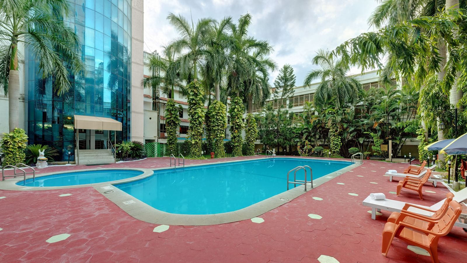 A swimming pool with trees and deck chair at SRM Hotel Maram Malai Nagar, Chennai