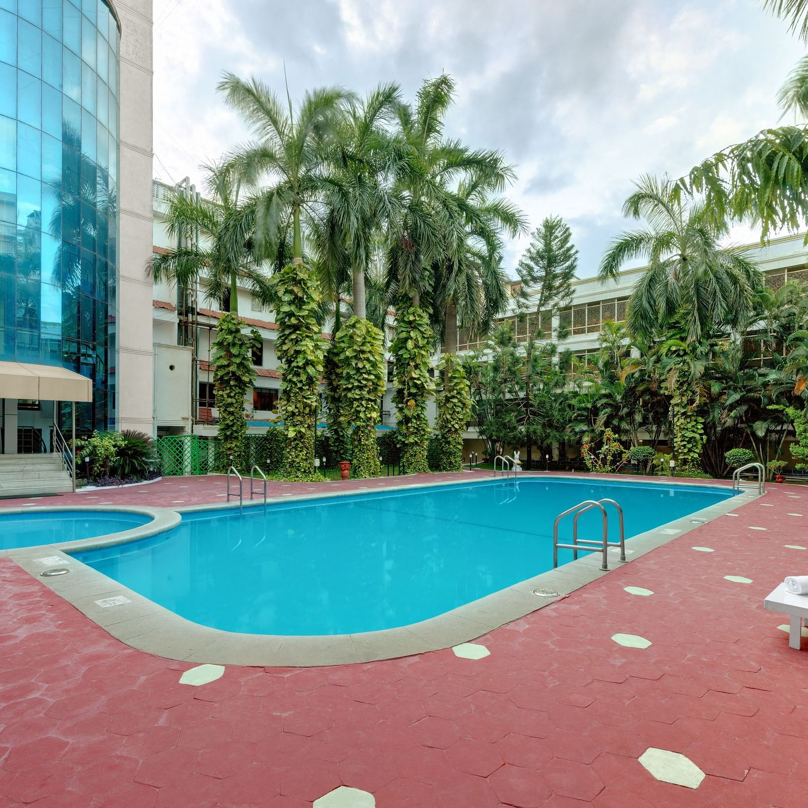 A swimming pool with trees and deck chair at SRM Hotel Maram Malai Nagar, Chennai