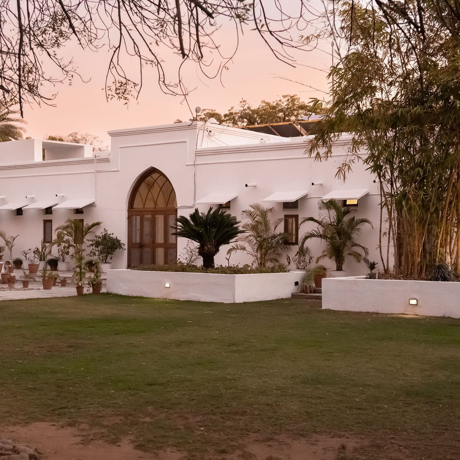 A single-story building with an arched doorway and a well-maintained lawn under a warm sky- Shahpura Bagh.