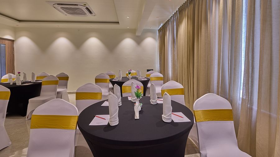 A banquet hall with chairs wrapped in white fabric and round tables covered in navy blue, illuminated by ambient lighting