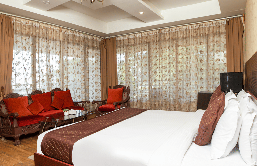 Bright bedroom featuring large windows, patterned curtains, and a well-made bed.