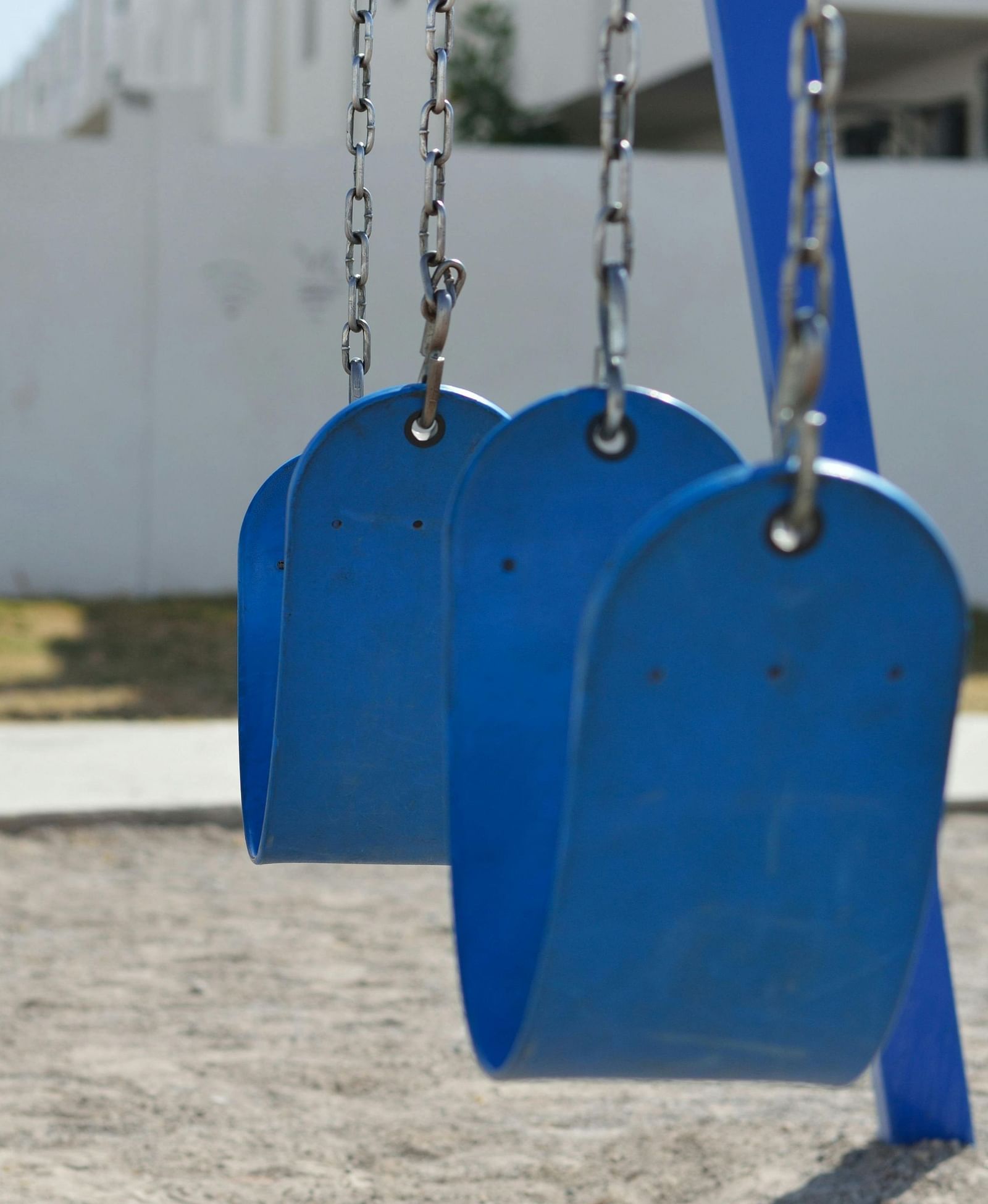 Children’s swing set with bright blue seats on sandy ground.