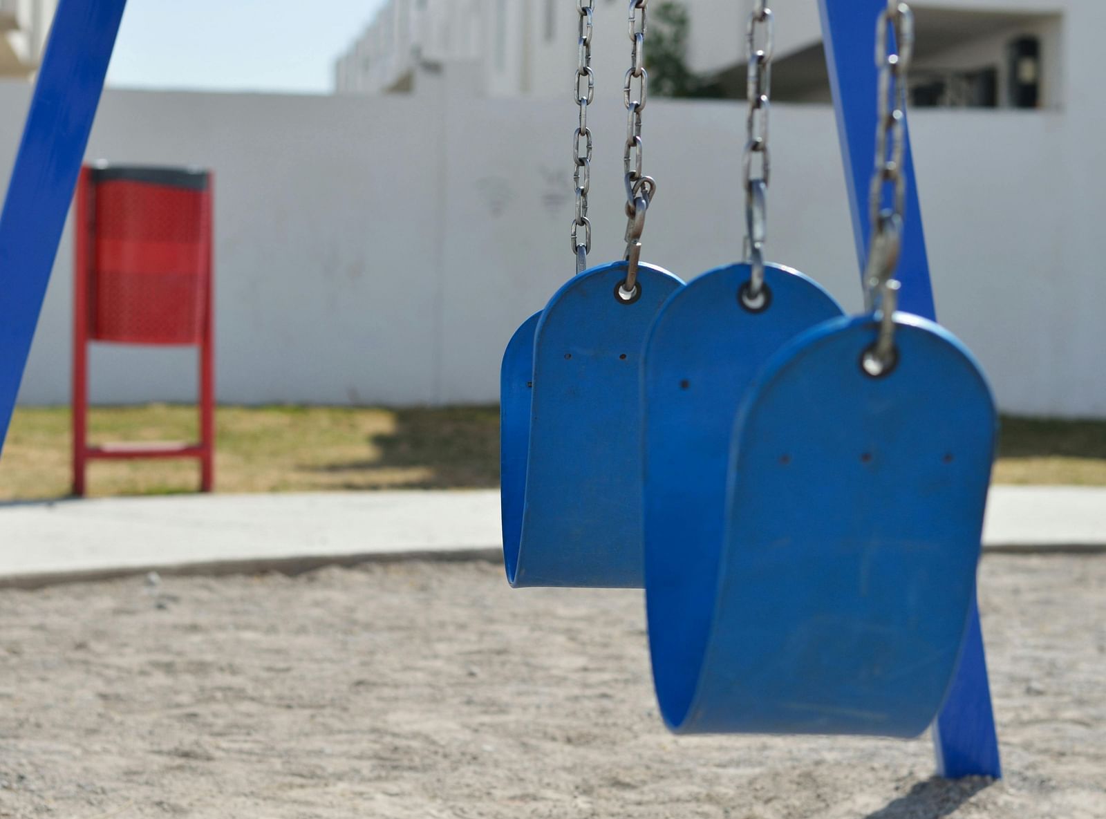 Children’s swing set with bright blue seats on sandy ground.