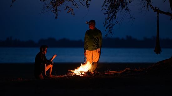 an image of a senior man and his friend warming his hands with the flames of a bonfire at cold weather in early morning