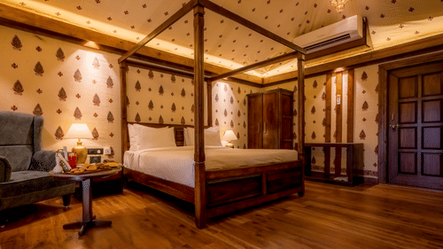 A Premium Tent accommodation space featuring poster bed, a sofa chair, a centre table with snacks and beverages, bedside table on either side with lamps, a wooden wardrobe, AC, and lot more at The Baagh Ananta Elite, Ranthambore