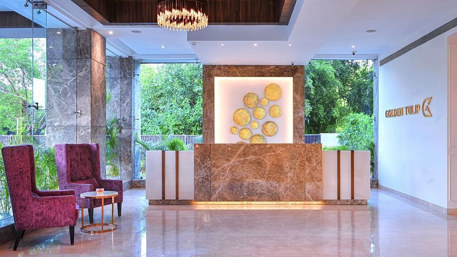 An image of a lobby area with a desk placed near two upholstered chair - Golden Tulip, Agra