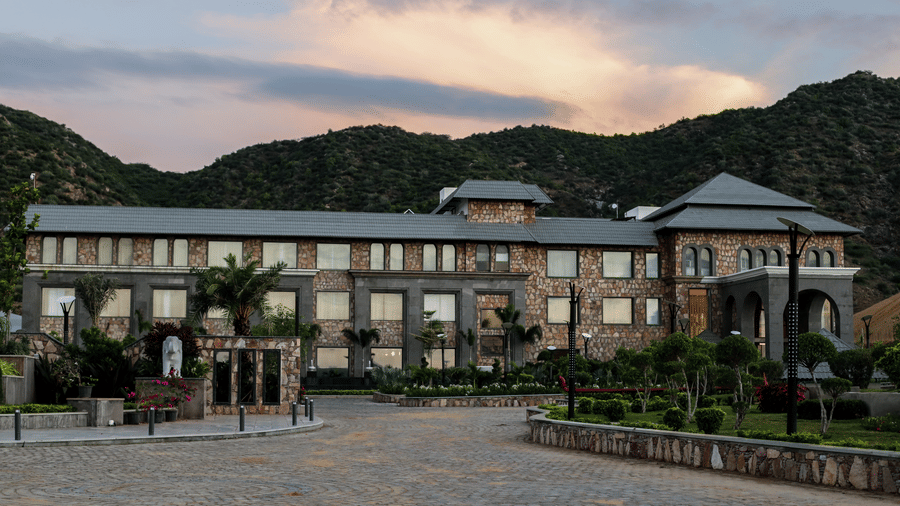 A different angle of the Pushkara Resort & Spa, Ajmer, with the driveway in the foreground and a warm, sunset-coloured sky - Pushkar Resorts Contact.