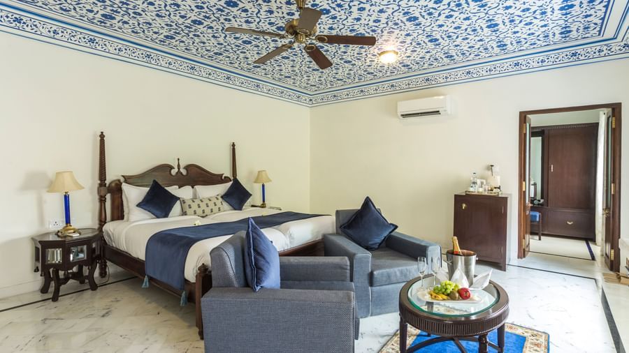 A bedroom at Royal Heritage Haveli with a four-poster bed, a seating area, and a ceiling with blue and white intricate patterns.