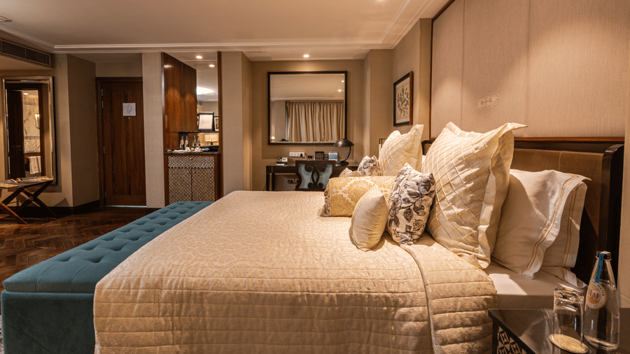 side view of the king sized bed at the cabana room with a work desk and a minibar at the far end of the room - The Claridges New Delhi
