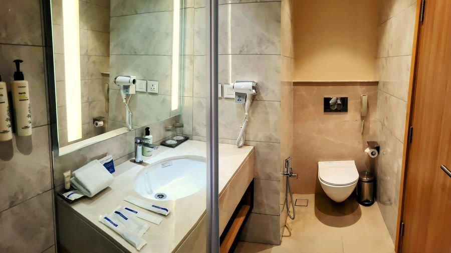 A view of a premium bathroom in the Executive Room at Golden Sarovar Portico, Amritsar, with a large, oval bathtub, a separate walk-in shower cubicle with a glass door, and a toilet.