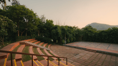 Open-air amphitheatre with curved seating, surrounded by lush greenery and hills.