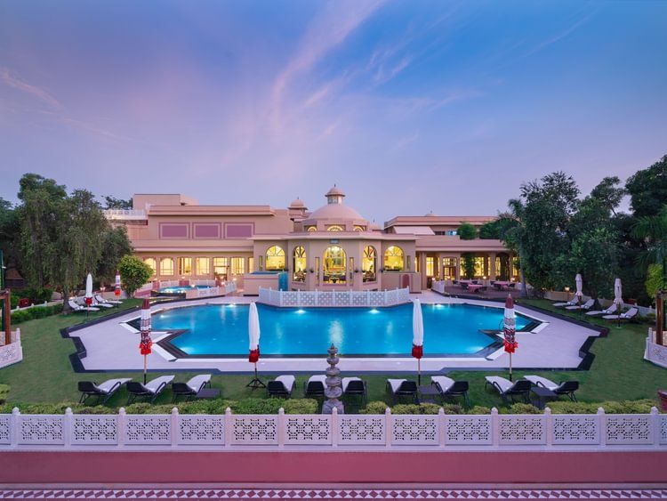 A lawn area with swimming pool surrounded by trees at Heritage Village Resorts & Spa.