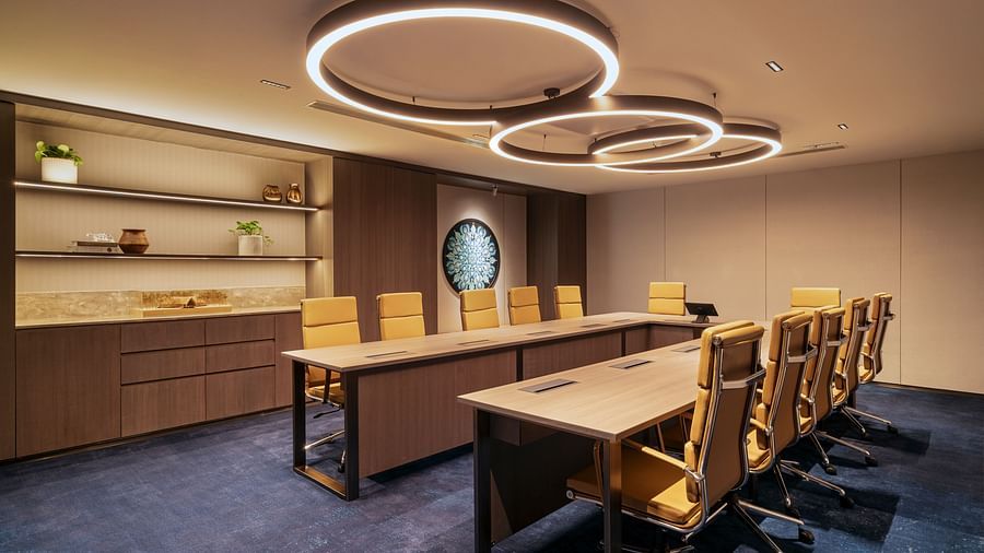 A meeting room at The Residency Towers Chennai with a long table, chairs, and modern circular lighting fixtures.