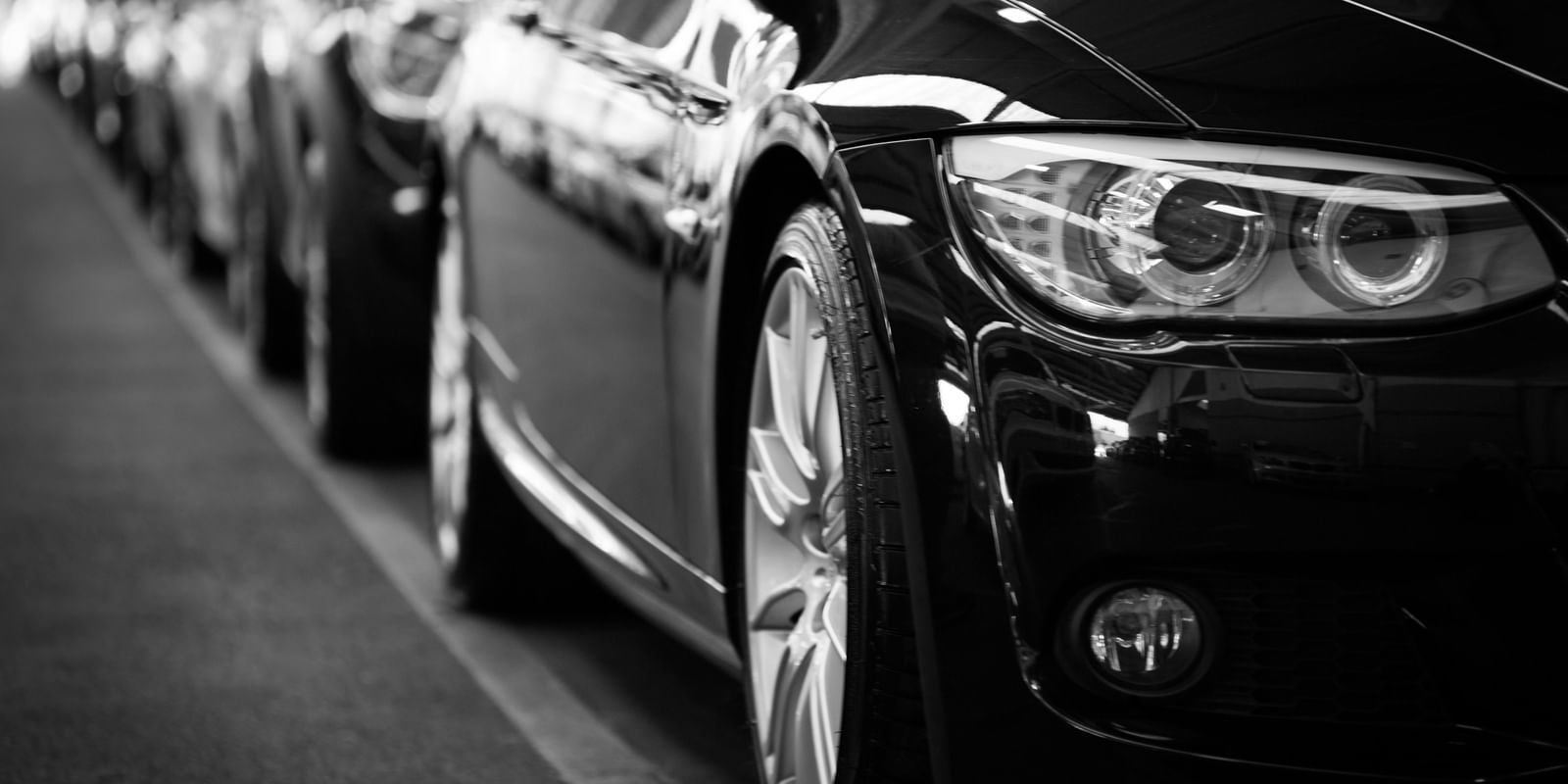 Headlights of a row of black car with the first cars alloy being projected.