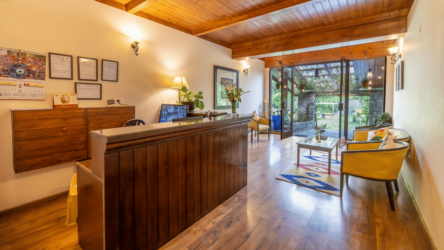 An image of a reception desk with lavish wooden interiors, wooden cabinets, chairs, etc.at Bedzzz Xclusiv Baikunth, Manali