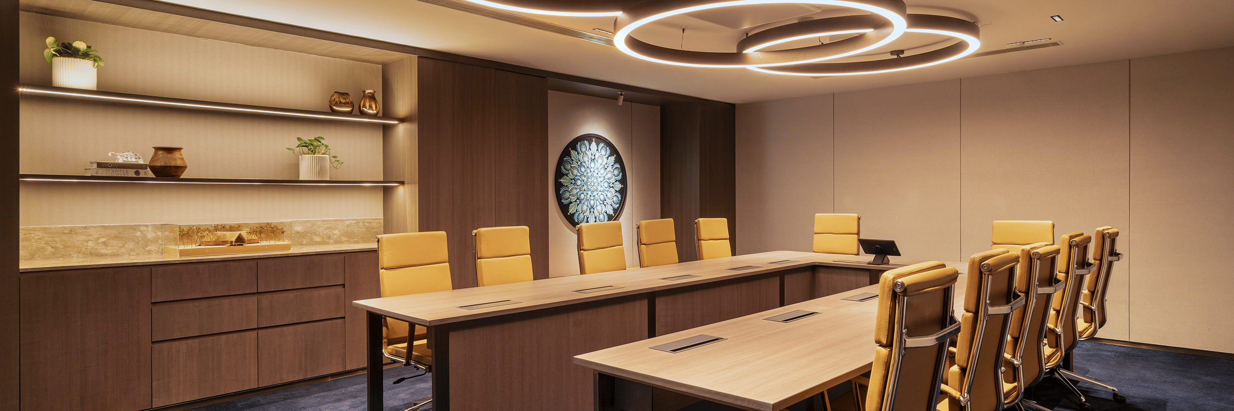 A meeting room at The Residency Towers Chennai with a long table, chairs, and modern circular lighting fixtures.