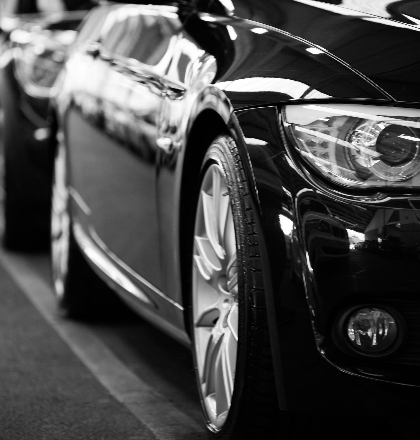 A close-up of the front of a black car, with other cars lined up behind it in a row.