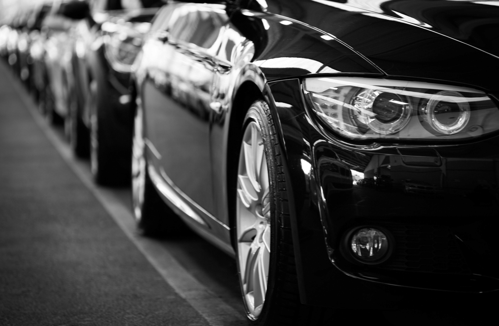 A perspective shot of a row of polished black luxury cars parked in a neat line outdoors.