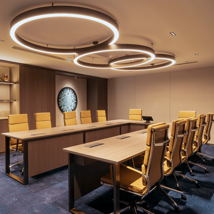 A meeting room at The Residency Towers Chennai with a long table, chairs, and modern circular lighting fixtures.