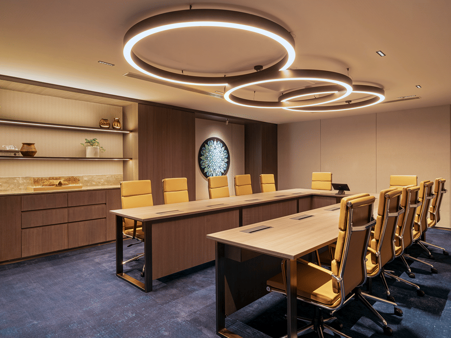 A meeting room at The Residency Towers Chennai with a long table, chairs, and modern circular lighting fixtures.