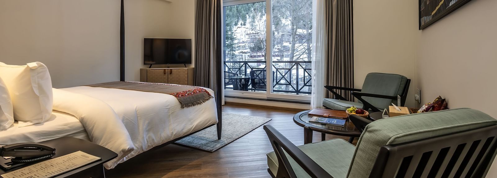 Bedroom with a four-poster bed, seating, and balcony area with mountain views at Nivasana Manali.