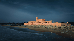 A tan stone building situated on a dark beach under a moody, overcast twilight sky.
